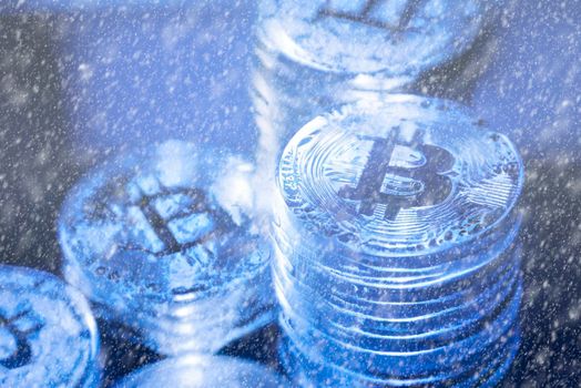Concept for Crypto winter, Bitcoin in blue ice. Bitcoin price crash. Horizontal view of cryptocurrency tokens, including Bitcoin, Ethererum Ripple, and Litecoin saw from above on blue shiny texture background
