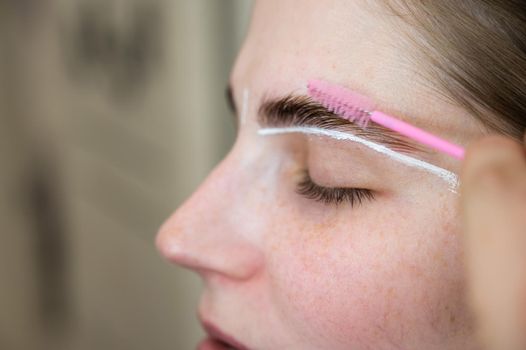 Close-up portrait caucasian woman combing her eyebrows