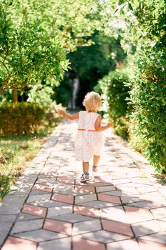 Little girl walks along the paving stones. Back view. High quality photo