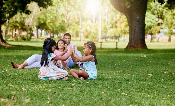 A happy asian couple lying together on grass outside, loving parents enjoy quality time with their little daughters playing a game. Couple bonding during family time at park with adopted foster sister.