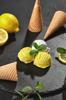 Close-up shot of a natural pleasant creamy and lemon ice cream decorated with sprigs of mint and served on a stone slate over a black background.