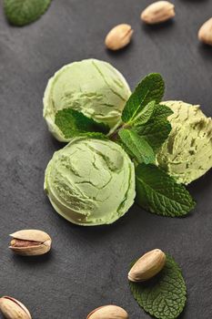 Top view of gourmet pistachio ice cream decorated with mint, scattered pistachios and served on a stone slate over a black background. Close-up.