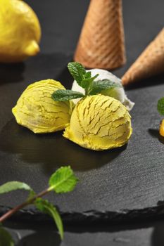 Close-up shot of a natural piquant creamy and lemon ice cream decorated with sprigs of mint and served on a stone slate over a black background.
