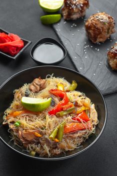 Chinese noodles with vegetables in a black plate. Asian rice or crystal noodles or glass noodles with vegetables. This is a classic Asian dish. Glass noodle with vegetable in a black bowl on a grey background. Asian food Asian cuisine. Asian or Szechuan noodles