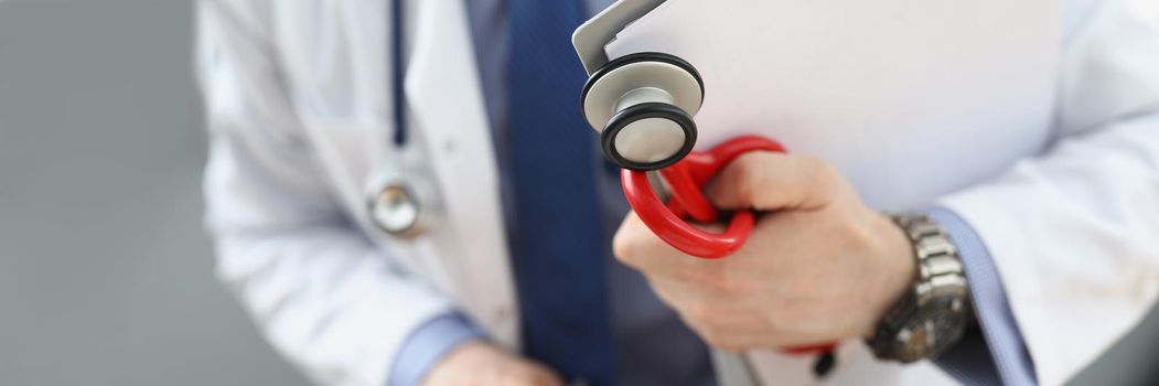 Close-up of doctor holding medical equipment red stethoscope and patient medical history. Medical building for health checkup. Medicine, clinic concept