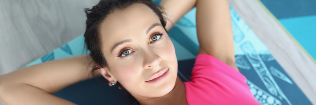 Top view of cute young woman in pink sportswear laying on mat for training. Take pause from exercises, chill on floor with hands under head. Break concept