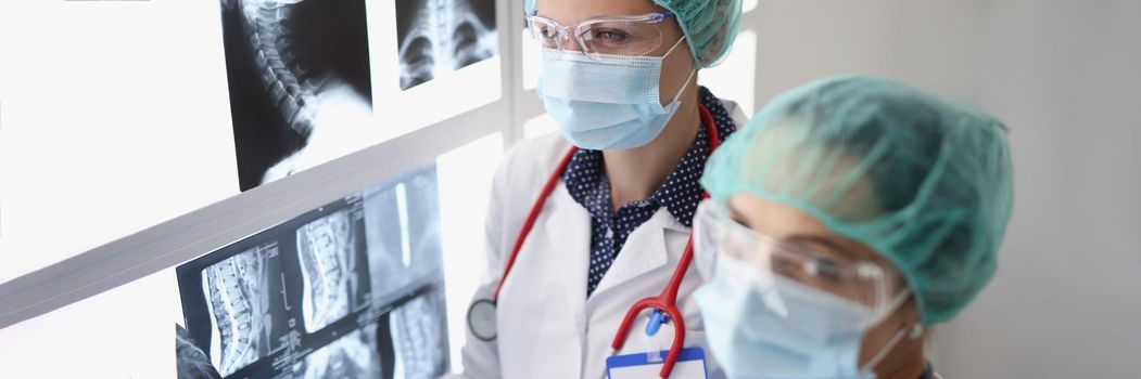 Portrait of women professional doctors look through x ray scans in hospital, examine patients result. Colleagues in protective uniform. Medicine concept