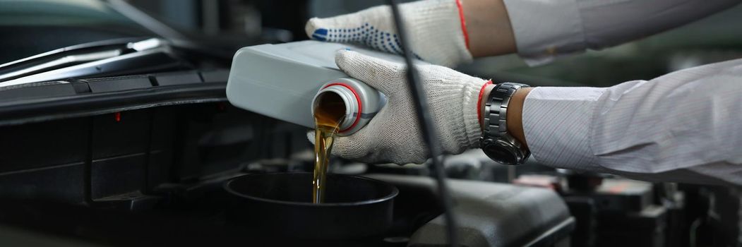 Close-up of worker refueling and pouring new oil into engine motor of automobile. Mechanic from maintenance service fix car. Maintenance, pit stop concept