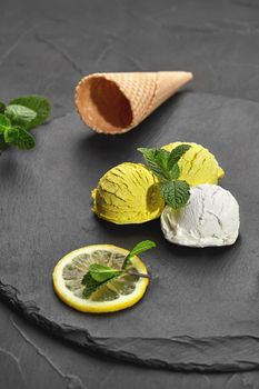 Close-up shot of a natural enjoyable creamy and lemon ice cream decorated with mint and served on a stone slate over a black background.