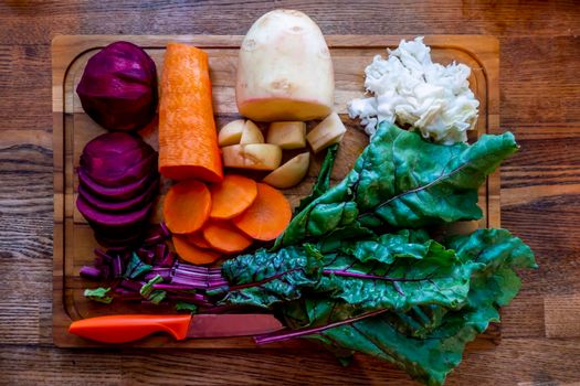 A board with ingredients for cooking delicious borscht on a wooden background. Cabbage, potatoes, carrots, beets with tops. Step-by-step process of slicing vegetables for beetroot soup High quality photo