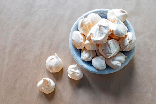 Homemade milk colored meringues on blue plate on crumpled craft paper. flatley composition: delicious homemade meringues on craft paper