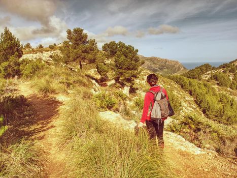 Hiker Woman With Backpack climb to view point in Mallorka island mountains. Rear view of middle-aged woman hiker looking mountains