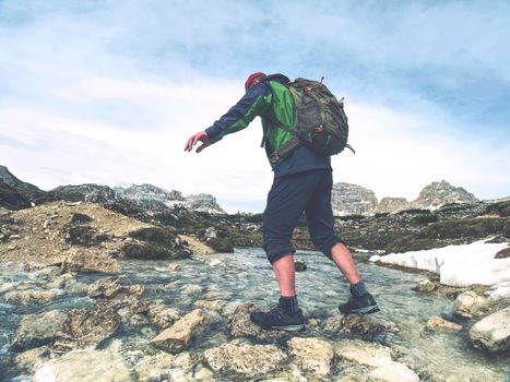 Man with backpack in trekking boots moves mountain river