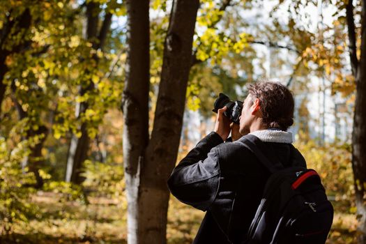 Young man photographer in jacket with backpack in forest taking pictures of nature