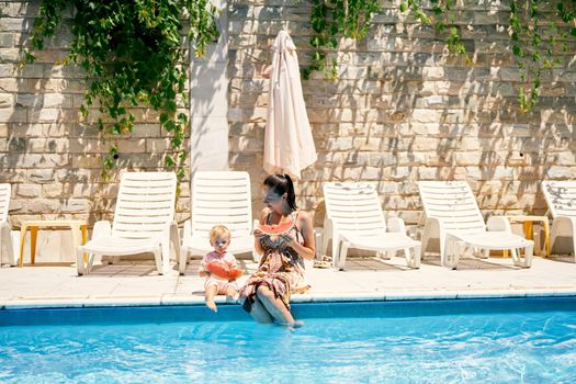 Mom and a little girl with pieces of watermelon in their hands are sitting by the pool. High quality photo