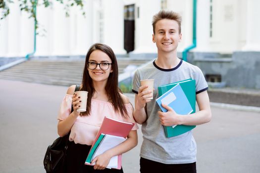 Young students with coffee and learning materials during break in front of university