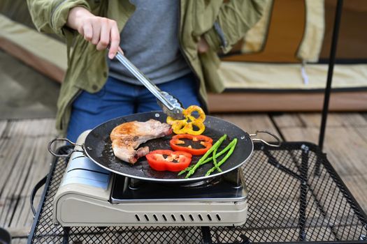 Cropped shot woman grilling meat on a portable gas stove during camping on summer holiday.