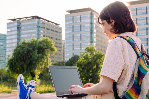 rear view of a young woman working in the city with her laptop and backpack, concept of technology, youth and digital nomad lifestyle, copy space for text