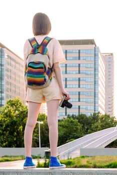 rear view of a young traveler woman with backpack and camera standing in front of the city, concept of youth and digital nomad lifestyle, vertical photo
