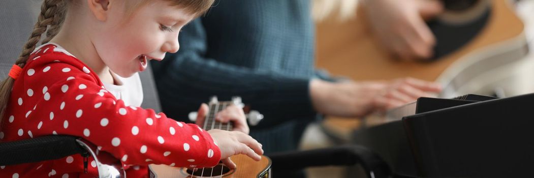 Portrait of happy child playing guitar, learn new song on musical instrument. Child sing and follow her female teacher. Preschool development, art concept