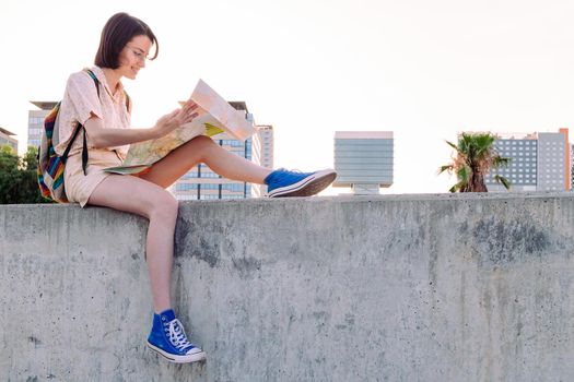 young traveler woman with backpack looking a map sitting in front of the city, concept of youth and nomad lifestyle, copy space for text
