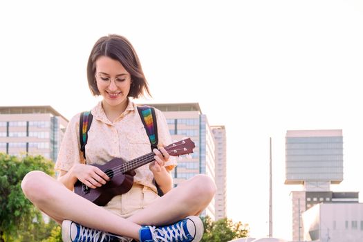 beautiful young woman in sneakers playing ukulele at sunset in the city, amateur music concept and artistic lifestyle, copy space for text