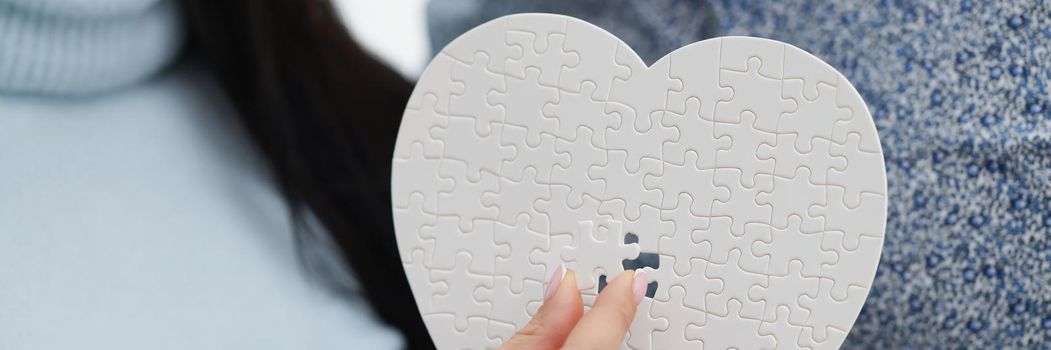 Close-up of woman fill empty space with missing piece of white heart puzzle, man holding it. Find missing detail as symbol for broken heart. Love concept