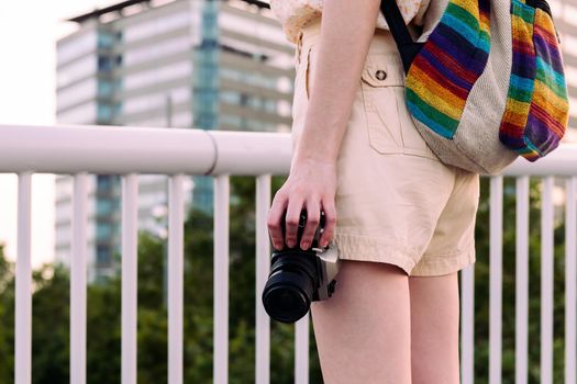 close-up of an unrecognizable young tourist woman with backpack in the city with a vintage camera in her hand, concept of youth and traveler lifestyle, copy space for text