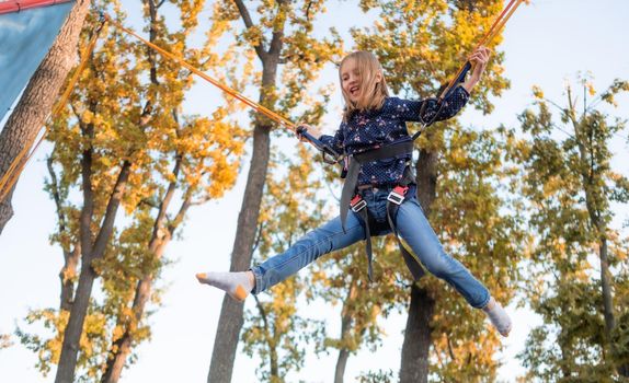 Excited little girl having fun on trampoline jumping rope at adventure park