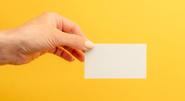 White business card with copy space in female hand on yellow background. Identity branding blank for contact information