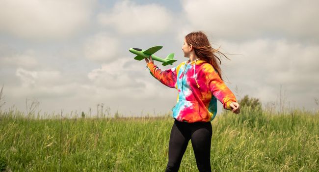 Beautiful teenager girl playing with toy plane outdoors in the field. Young female person launching airplane at the nature. Concept of freedom