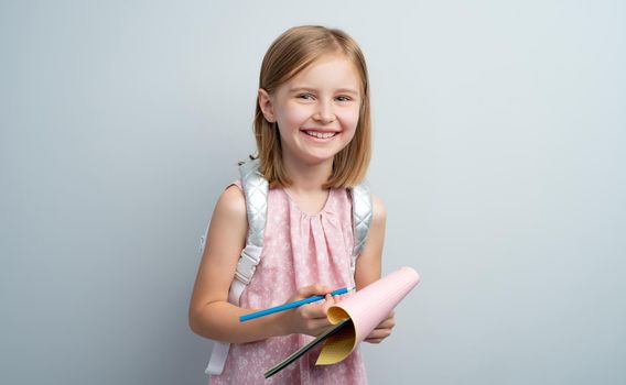 Little girl taking notes in notebook using colored pencil