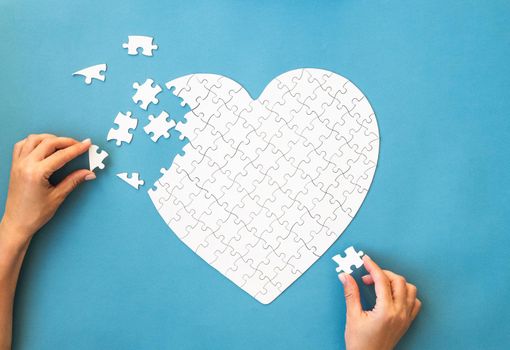 White puzzle in heart shape. White details of puzzle on blue background. Romantic concept.