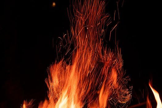 Campfire flame stripes flying to the dark night sky. Orange fire sparks isolated on black background