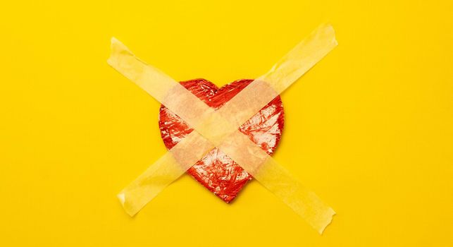 Red heart sticked up with masking tape isolated on yellow background with copyspace. Concept of fear to love and trust again, symbol of lonely person with broken feelings