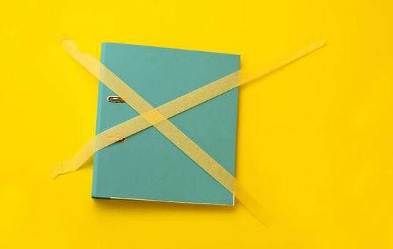 Folder sticked up with masking tape isolated on yellow background with copyspace. Concept of forbidden knowledge, security and safety of information