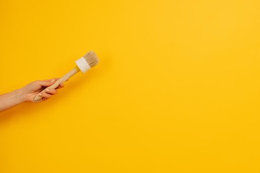 Woman hand holding wooden paint brush on yellow background with copy space. Working tool for home design project