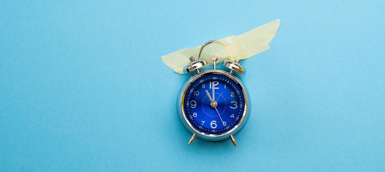 Designed clock with masking tape isolated on blue background with copy space. Concept of time value. Weekend morning without work hours