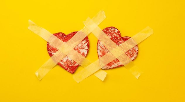 Two red hearts sticked up with masking tape isolated on yellow background with copyspace. Concept of broken relationships, fear to love and trust again, symbol of lonely person