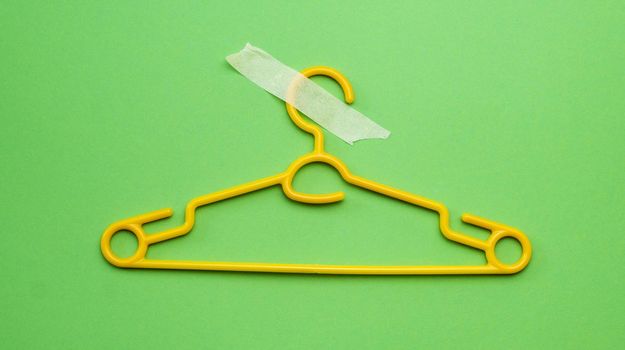 Hanger with masking tape isolated on green background with copy space. Concept of sales, fashion and e-commerce retail world. Equipment for clothes