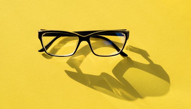 Blck glasses isolated on yellow background with copyspace. Concept of eyesight and vision. Modern optical frame googles accessory