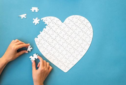 White puzzle in heart shape. White details of puzzle on blue background in girls hands. Romantic concept.