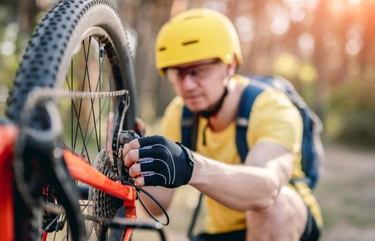 Cyclist checking chainwheel defect on upside down bicycle in forest