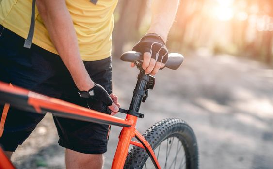 Man adjusting bicycle seat height outdoors in forest