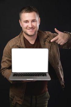 Handsome smiling bearded man holding his laptop and pointing with his index finger at copy space. studio shot.