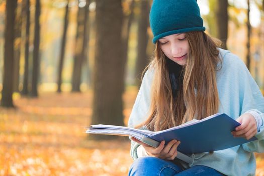 Nice student reading textbook on natural autumn background