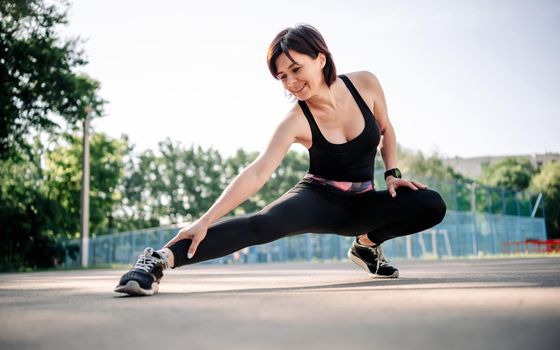 Beautiful Young girl woman doing stretching outdoors preparing for fitness workout. Female exercising at stadium in summer time. Portrait of adult girl during sport training