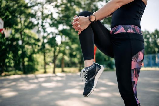 Young girl woman stretching her legs at stadium during fitness workout. Female person wearing sport outfit exercising outdoors