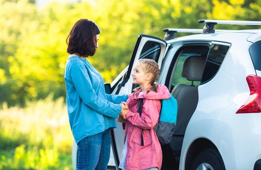 Mother taking primary schoolgirl back to school saying goodbye at parking