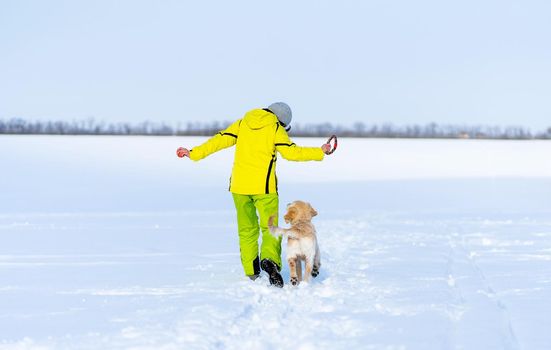 Back view of beautiful young retriever dog with owner on snowy field